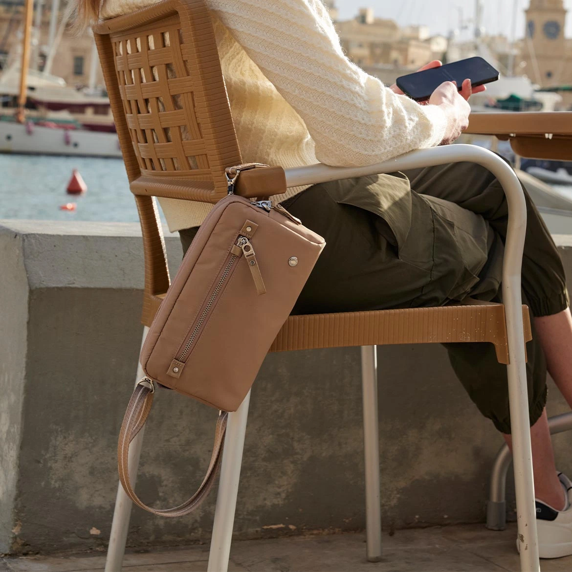 Elegancska torebka z serii Pacsafe W wkolorze beżowym przypięta karabińczymkiem Turn'N'Lock do krzesełka